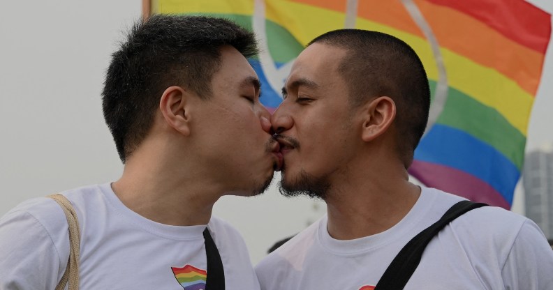 A queer or gay couple sharing a kiss in front of an LGBTQ Pride flag