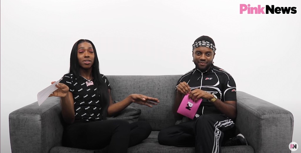 This is an image of two Black men sitting on a couch in a white room. 