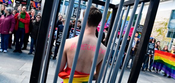 An activist stands naked, wrapped in a rainbow flag, in a mock cage in front of the Chancellery in Berlin on April 30, 2017, during a demonstration calling on Russian President to put an end to the persecution of gay men in Chechnya.