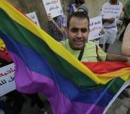 A protestor waves the gay pride flag as others hold banners during an anti-homophobia rally in Beirut on April 30, 2013. Lebanese homosexuals, human rights activists and members from the NGO Helem (the Arabic acronym of "Lebanese Protection for Lesbians, Gays, Bisexuals and Transgenders") rallied to condemn the arrest on the weekend of three gay men and one transgender civilian in the town of Dekwaneh east of Beirut at a nightclub who were allegedly verbally and sexually harassed at the municipality headquarters. AFP PHOTO/JOSEPH EID (Photo credit should read JOSEPH EID/AFP/Getty Images)