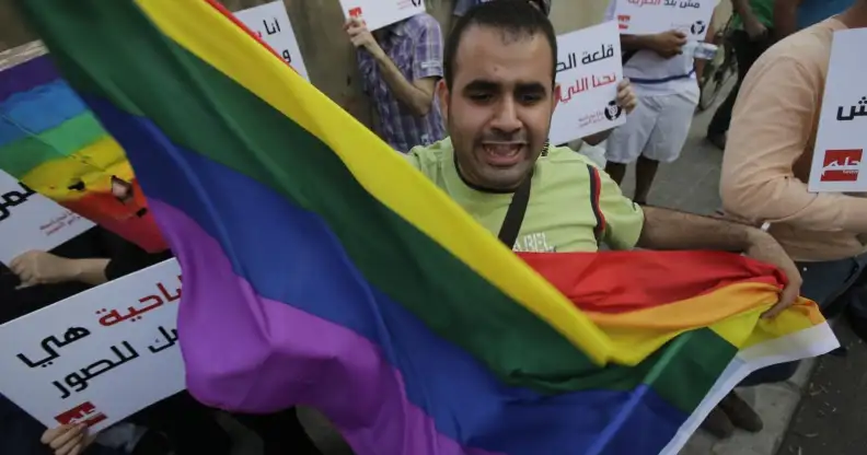A protestor waves the gay pride flag as others hold banners during an anti-homophobia rally in Beirut on April 30, 2013. Lebanese homosexuals, human rights activists and members from the NGO Helem (the Arabic acronym of "Lebanese Protection for Lesbians, Gays, Bisexuals and Transgenders") rallied to condemn the arrest on the weekend of three gay men and one transgender civilian in the town of Dekwaneh east of Beirut at a nightclub who were allegedly verbally and sexually harassed at the municipality headquarters. AFP PHOTO/JOSEPH EID (Photo credit should read JOSEPH EID/AFP/Getty Images)