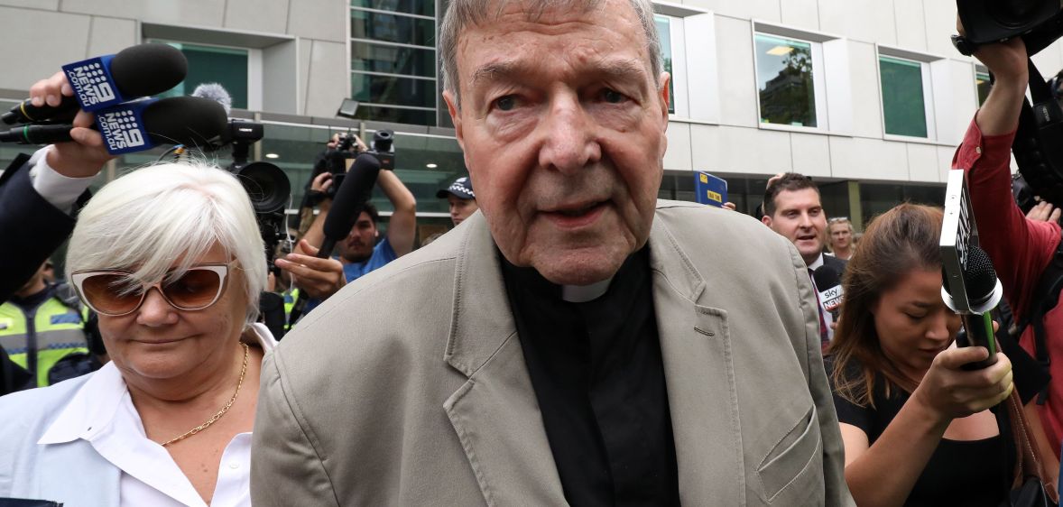 Photo of Cardinal George Pell wearing a gret suit jacket over a black shirt as he leaves Victoria county court in Melbourne surrounded by photographers
