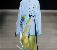 Tales Soares walking a catwalk in a blue shirt and green trousers