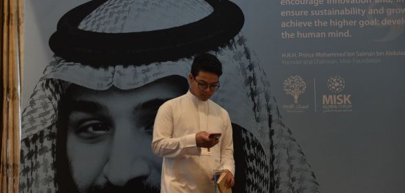 A young man in Saudi Arabia, where textbooks teach gay sex is punishable by death, stands in front of a portrait of Saudi Crown Prince Mohammed bin Salman.