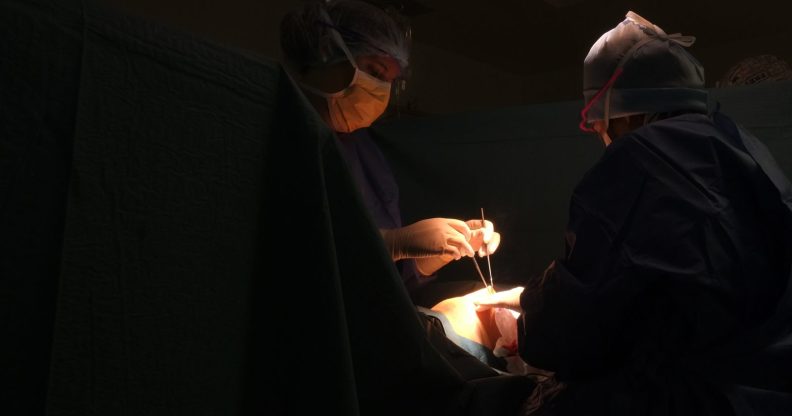 Two surgeons operate on someone in a dark room