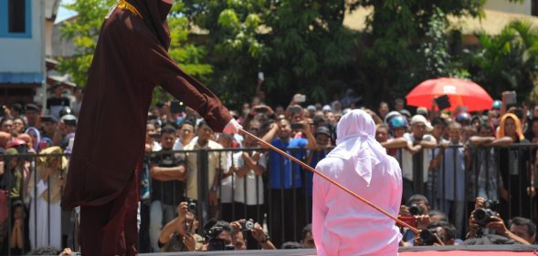 A religious officer canes an Acehnese youth onstage as punishment for dating outside of marriage, which is against sharia law, outside a mosque in Banda Aceh on August 1, 2016. The strictly Muslim province, Aceh has become increasingly conservative in recent years and is the only one in Indonesia implementing Sharia law. / AFP / CHAIDEER MAHYUDDIN (Photo credit should read CHAIDEER MAHYUDDIN/AFP/Getty Images)