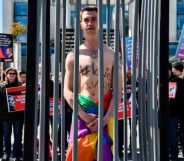 An activist stands naked, wrapped in a rainbow flag, in a mock cage