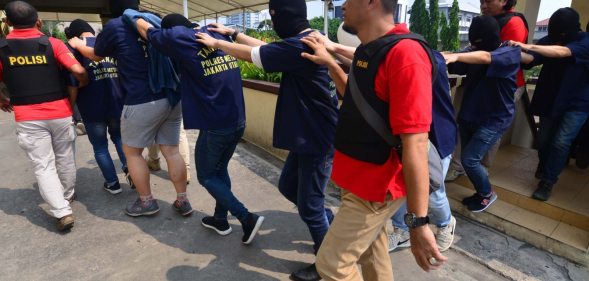 Indonesian police guard men arrested in a recent raid during a press conference at a police station in Jakarta on May 22, 2017. Indonesian police have detained 141 men who were allegedly holding a gay party at a sauna, an official said on May 22, the latest sign of a backlash against homosexuals in the Muslim-majority country