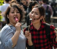 KAWASAKI, JAPAN - APRIL 01: (EDITORS NOTE: Image contains suggestive content.) Women react to the camera as they eat phallic-shaped lollipops during Kanamara Matsuri (Festival of the Steel Phallus) on April 1, 2018 in Kawasaki, Japan. The Kanamara Festival is held annually on the first Sunday of April. The penis is the central theme of the festival, focused at the local penis-venerating shrine which was once frequented by prostitutes who came to pray for business prosperity and protection against sexually transmitted diseases. Today the festival has become a popular tourist attraction and is used to raise money for HIV awareness and research. (Photo by Carl Court/Getty Images)