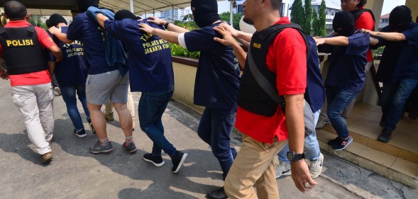 Indonesian police guard men arrested in a recent raid during a press conference at a police station in Jakarta on May 22, 2017. Indonesian police have detained 141 men who were allegedly holding a gay party at a sauna, an official said on May 22, the latest sign of a backlash against homosexuals in the Muslim-majority country. / AFP PHOTO / FERNANDO (Photo credit should read FERNANDO/AFP/Getty Images)
