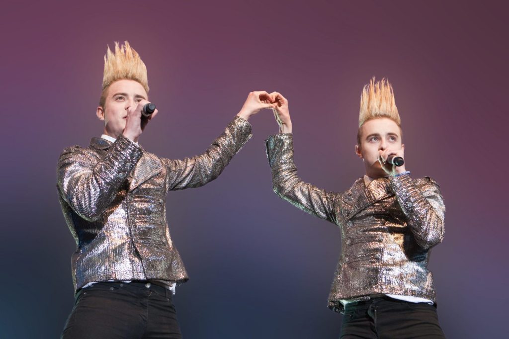 Jedward performing together on stage with silver jackets