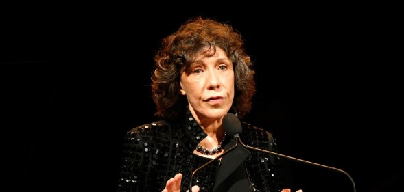 Lily Tomlin in a black sequinned jacket speaking into a microphone