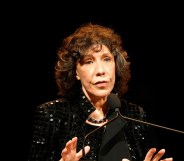 Lily Tomlin in a black sequinned jacket speaking into a microphone