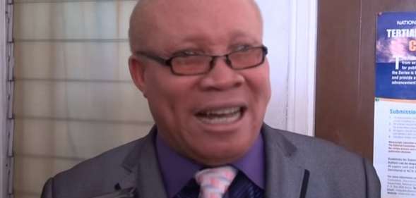 Moses Foh-Amoaning in a purple shirt and grey blazer talking to the camera