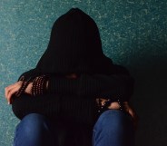 A teenager sits with their face covered by a black hoodie