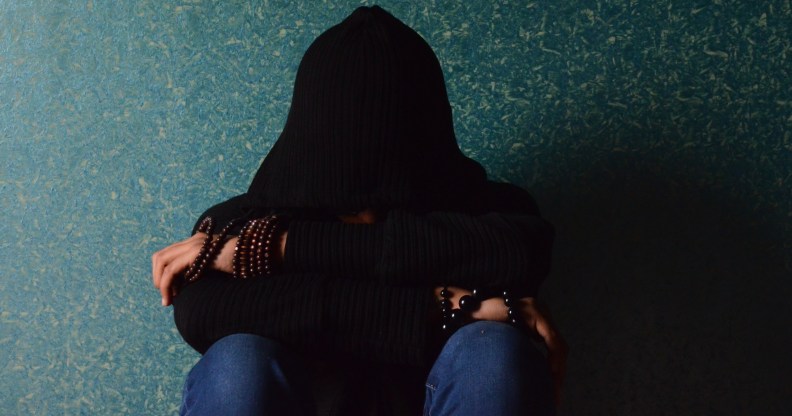 A teenager sits with their face covered by a black hoodie