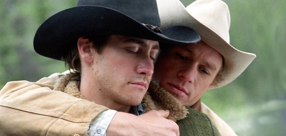 A still from the 2005 film Brokeback Mountain showing actors Jake Gyllenhaal and Heath Ledger dressed in their cowboy outfits with Ledger standing close to Gyllenhaal with his arm around him
