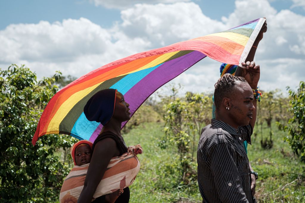 Two LGBT+ refugees and a child march holding a rainbow flag