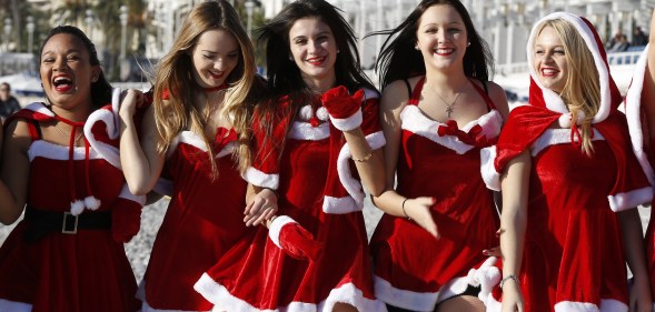 Young women dressed in Santa Claus outfit pose within the traditional Christmas bath on a beach in downtown Nice