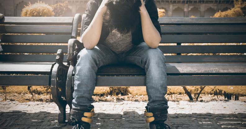 Boy holds his head in his hands as he sits on a bench