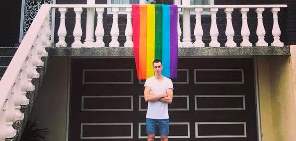 Daniel Comesoli outside of his apartment with a rainbow hanging from his balcony.