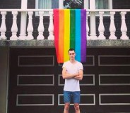 Daniel Comesoli outside of his apartment with a rainbow hanging from his balcony.