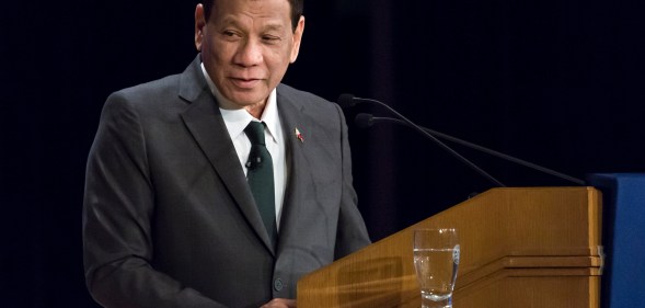 Rodrigo Duterte speaking at a lectern, wearing a black suit and tie