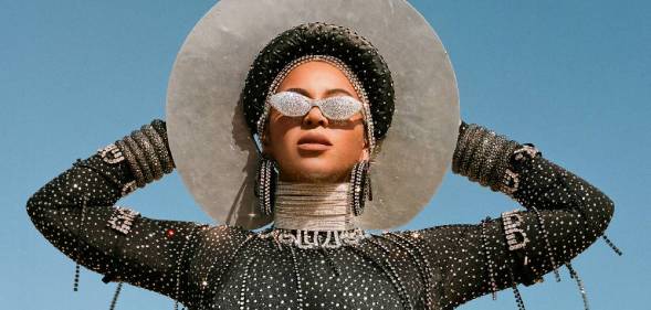 Beyoncé in Black is King wearing bejewelled sunglasses, a white wide-brimmed hat and a sparkly black body stocking