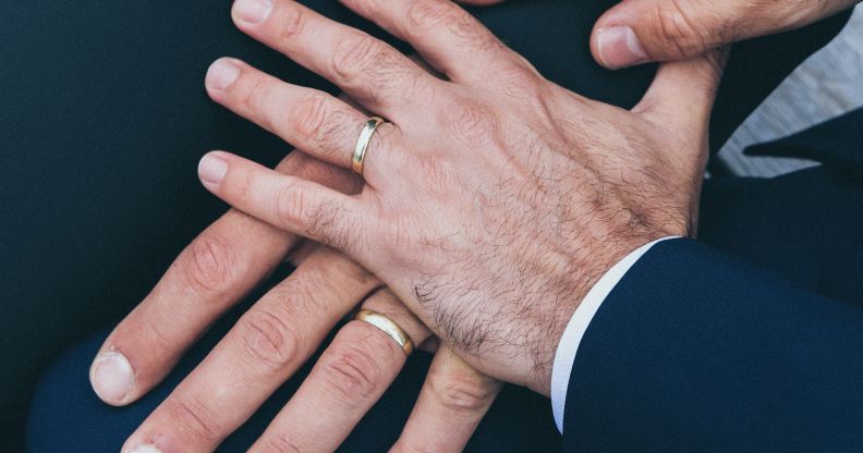 Two male hands touching, both wearing wedding rings