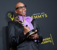 RuPaul holding his Emmy Award, wearing a black jacket and a purple pussy bow