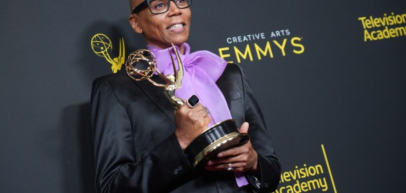 RuPaul holding his Emmy Award, wearing a black jacket and a purple pussy bow