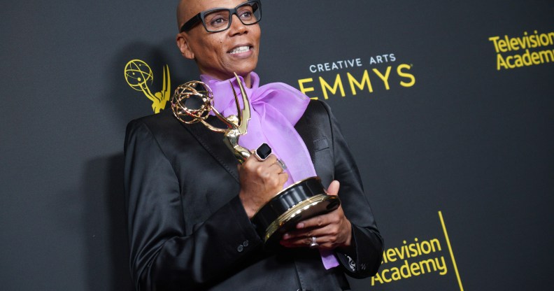 RuPaul holding his Emmy Award, wearing a black jacket and a purple pussy bow