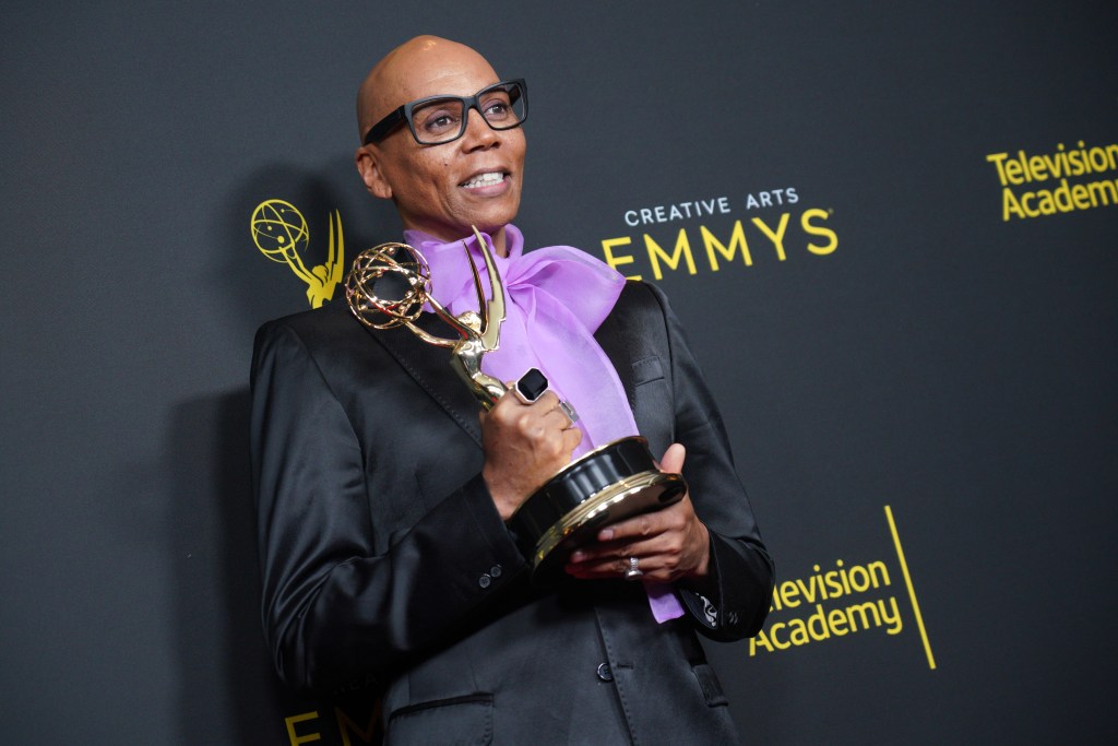 RuPaul holding his Emmy Award, wearing a black jacket and a purple pussy bow