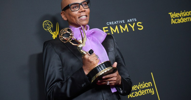 RuPaul holding his Emmy Award, wearing a black jacket and a purple pussy bow