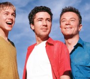 Nathan, Stuart and Vince from Queer as Folk, smiling against a blue sky