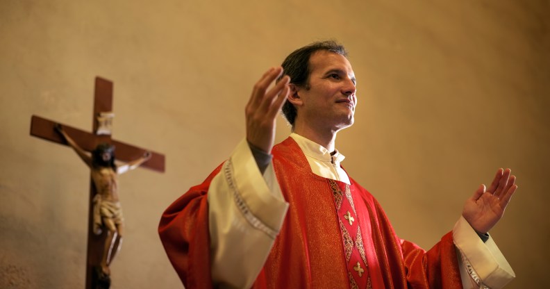 Catholic priest on altar praying with open arms during mass service in church. (Stock photo via Elements Envato)