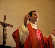 Catholic priest on altar praying with open arms during mass service in church. (Stock photo via Elements Envato)