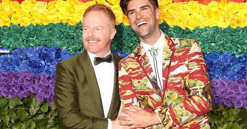 Modern Family Jesse Tyler Ferguson and his husband Justin Mikita in front of a rainbow flower wall