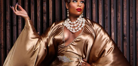 A promo of RuPaul's Drag Race showing drag queen Peppermint wearing a gold dress and over-the-top white pearl necklace posing in front of a dark wooden background