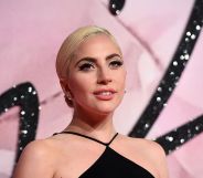 Lady Gaga poses against a pink background in a black dress