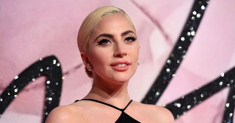 Lady Gaga poses against a pink background in a black dress