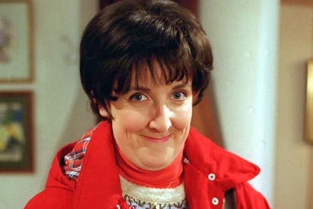 Hayley Cropper, wearing a red coat with short dark hair