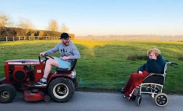 Tommy Ferris tows his grandmother's wheelchair on his sit-down lawnmower. (Screen capture via BBC)
