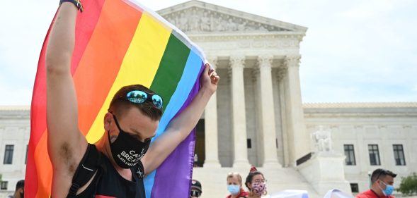 A man waves a rainbow flag in front of the Supreme Court.