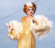 Biance Del Rio in a gold sequinned wrap dress and fur shrug, on the cusp of telling a joke