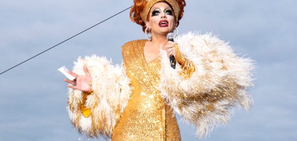 Biance Del Rio in a gold sequinned wrap dress and fur shrug, on the cusp of telling a joke