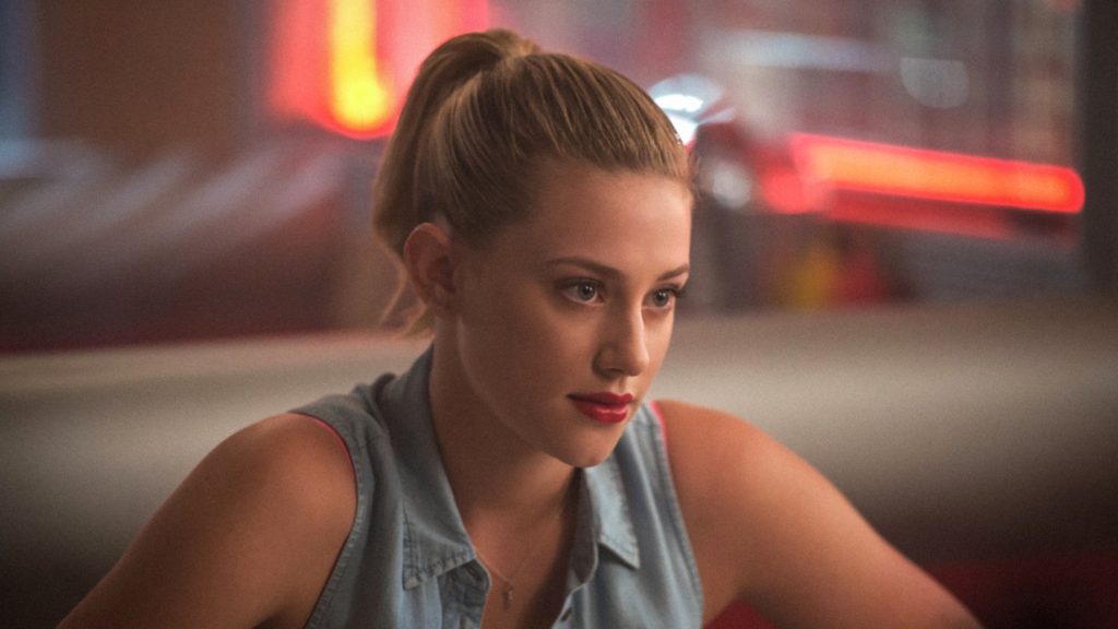 Lili Reinhart as Betty Cooper in Riverdale, wearing a sleeveless denim shirt, red lipstick and a ponytail