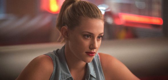 Lili Reinhart as Betty Cooper in Riverdale, wearing a sleeveless denim shirt, red lipstick and a ponytail