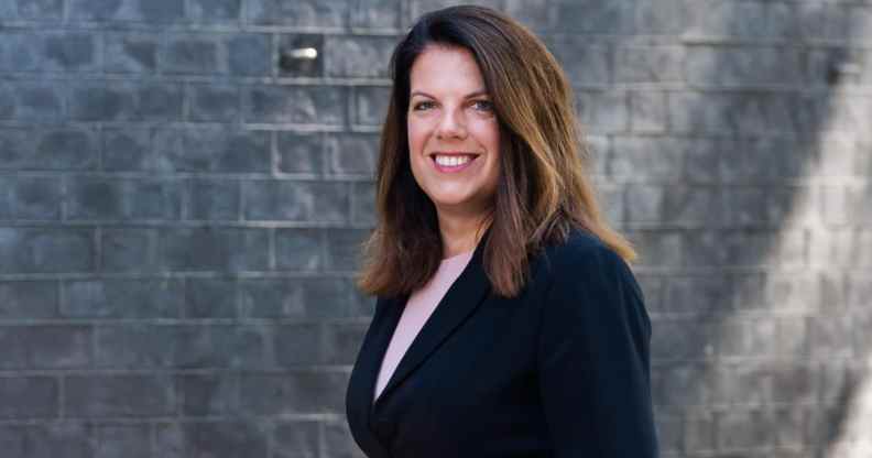 Photo of Conservative MP Caroline Nokes wearing a black suit standing in front of a grey brick wall