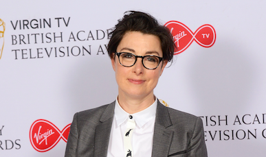 A photo of TV presenter Sue Perkins wearing a white shirt and silver grey suit jacket as she smiles to the camera during the British Academy Television Awards